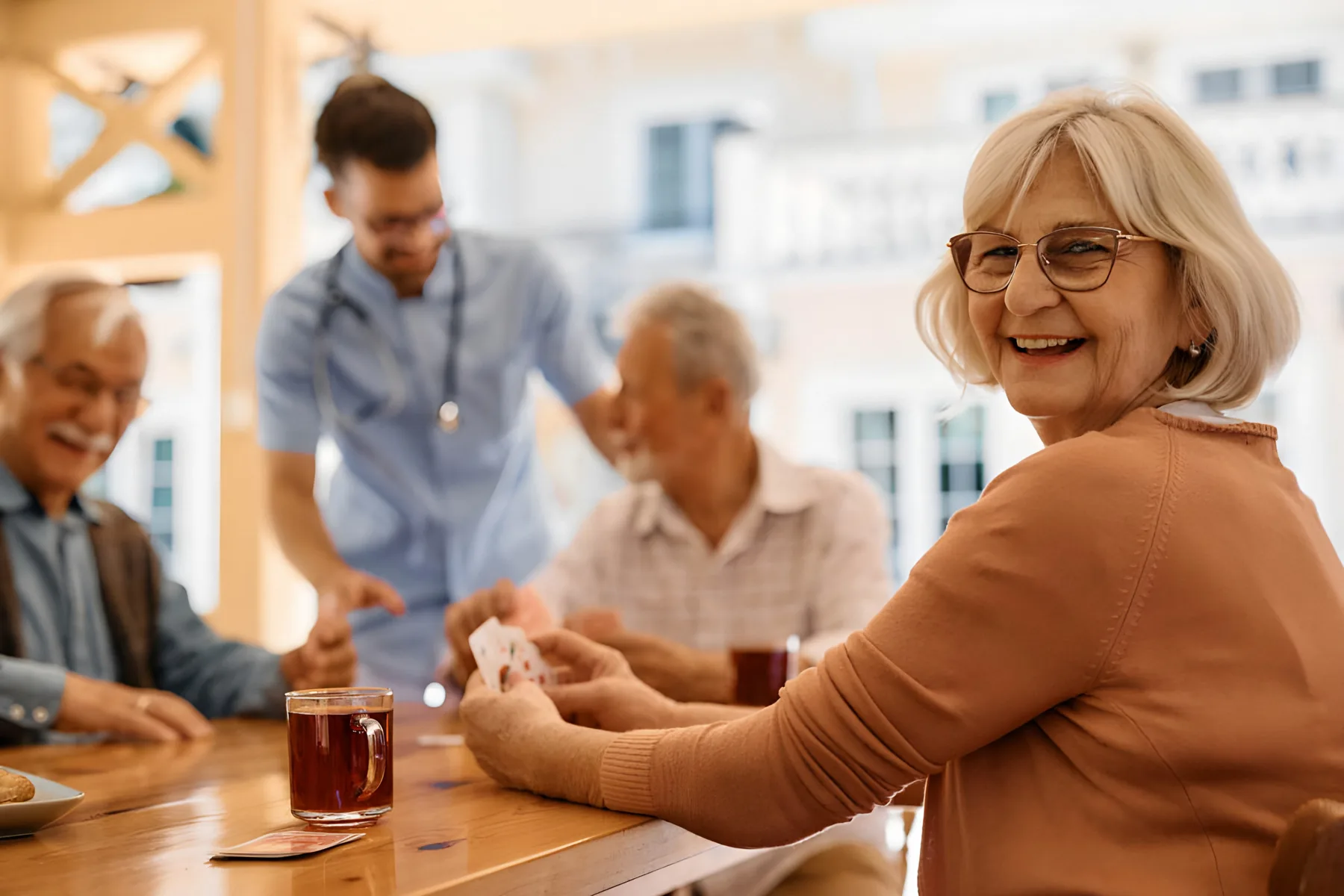 Residents playing cards at a table while a nurse looks on