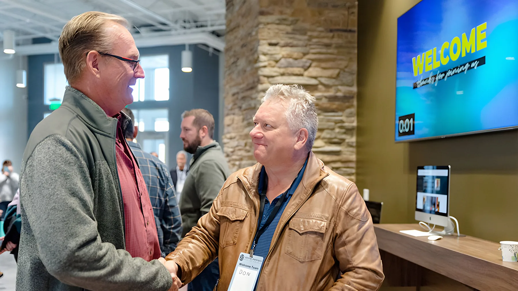 Two men shaking hands in the church lobby under a welcome screen