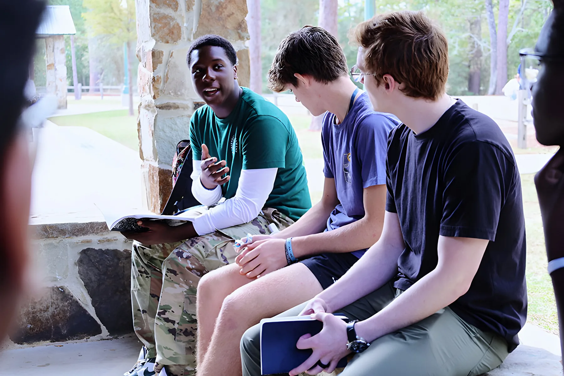 Three students talking outdoors with a Bible open