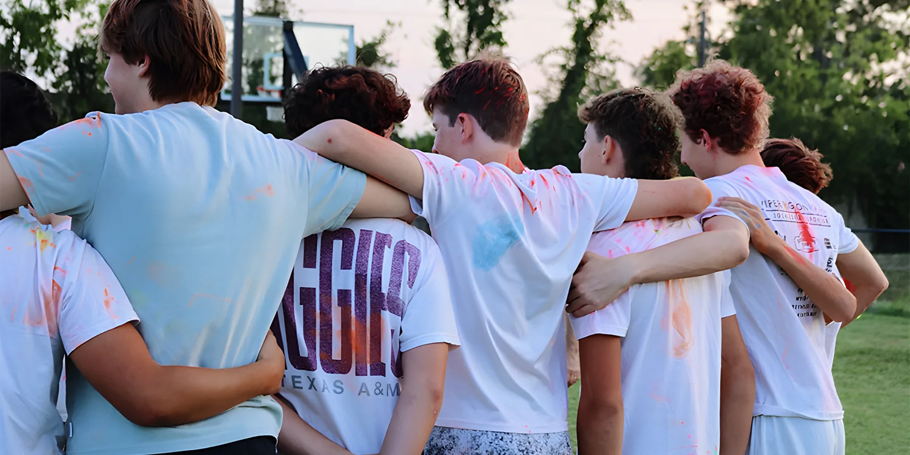 Students standing arm in arm, their shirts covered in colored powder